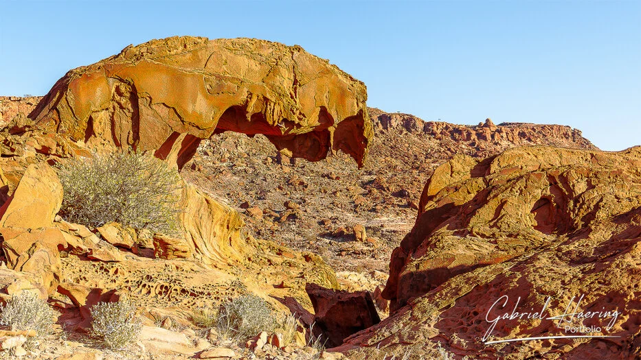 Golden rock formations and dry desert vegetation in the rugged landscape of Damaraland, Namibia