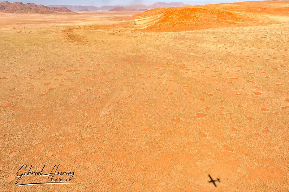 Wide aerial landscape with fairy circles, red dunes and distant mountains in the Namib-Naukluft region of Namibia