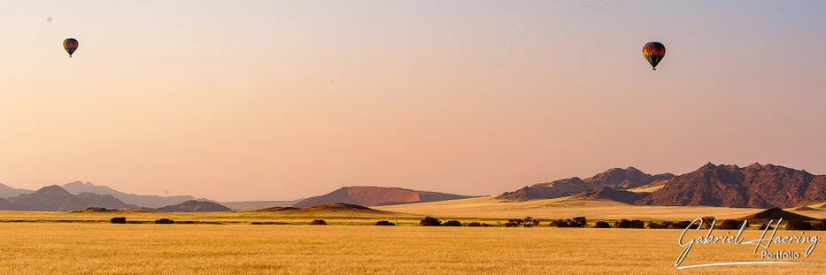 Hot air balloons flying at sunrise above the desert plains and mountains of Namib-Naukluft, Namibia