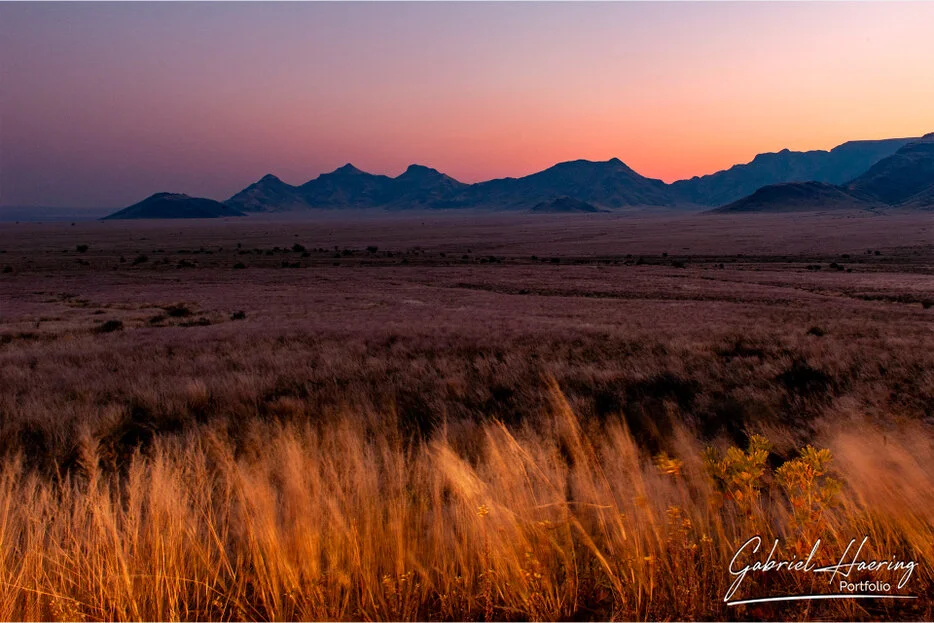 Sunset over dry desert grasslands and mountain silhouettes in Namib-Naukluft National Park, Namibia